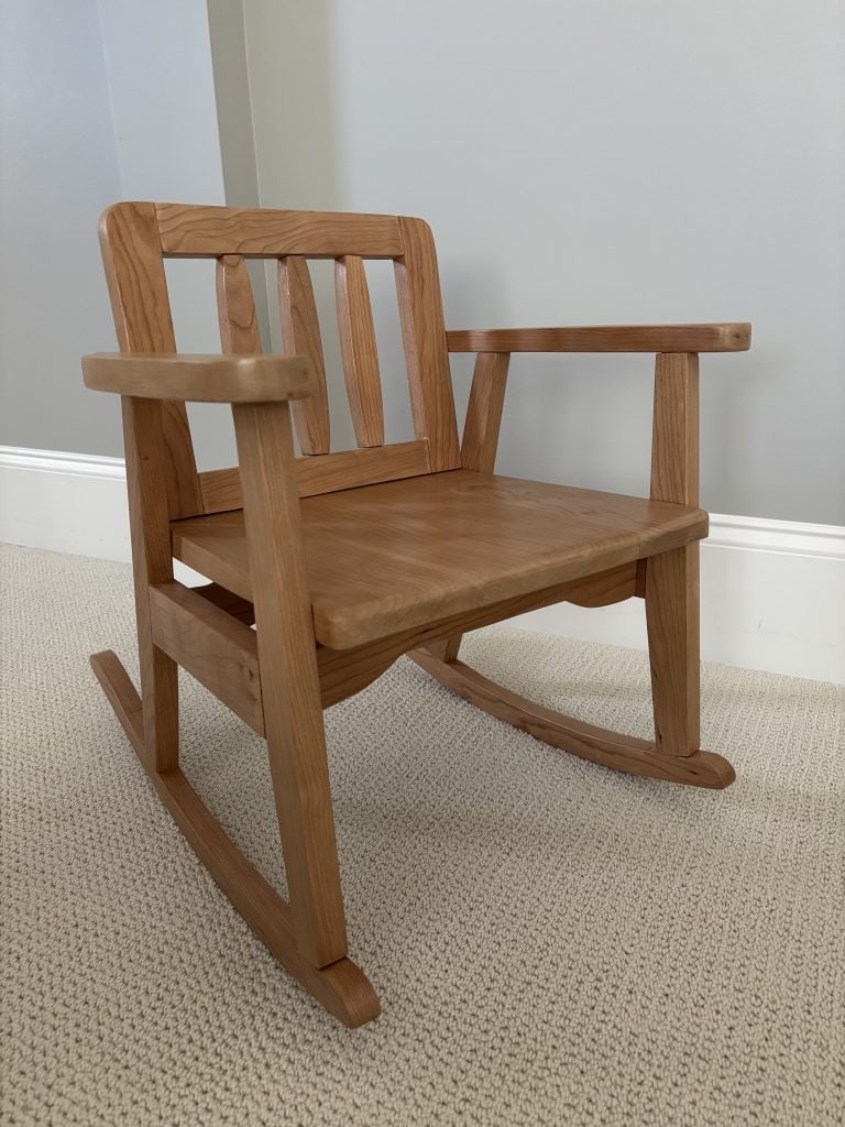 The companion child's rocking chair in cherry, with slat back, shaped seat and curved arms.