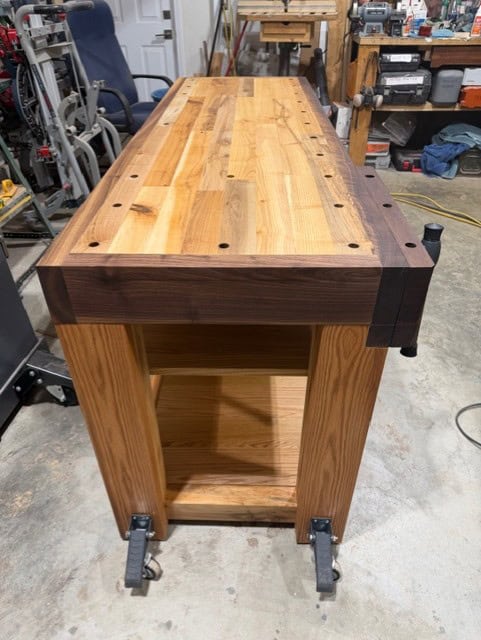 End view of the finished bench, showing the walnut end cap, the vise hardware and the lower shelf.