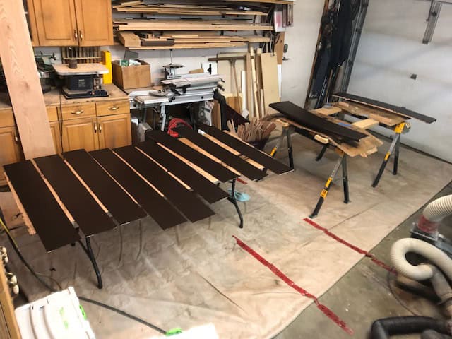 Stained risers and treads laid out on sawhorses and sticks to dry in the garage.