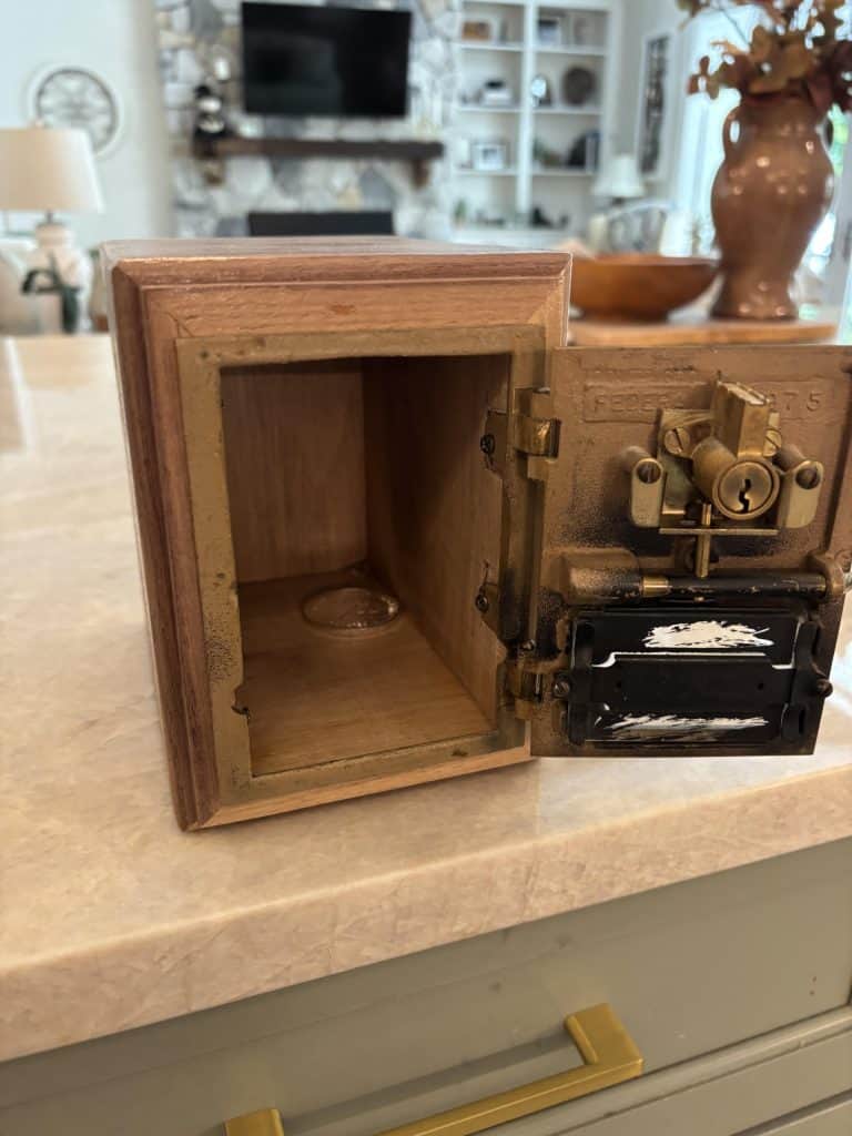 The key-operated bank with its door swung open. Dave mortised the hinge leaves into the walnut side so the short screws get a full bite, and a coin dropped through the slot sits inside.
